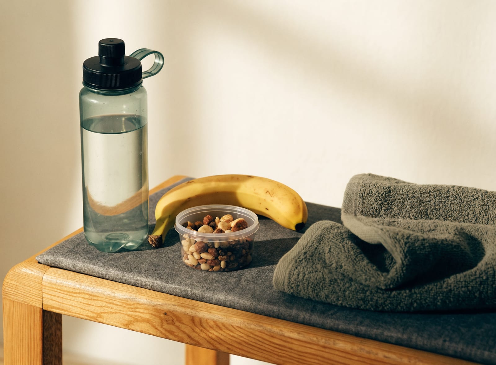 Green water bottle, banana, and trail mix laid out on a bench with towels