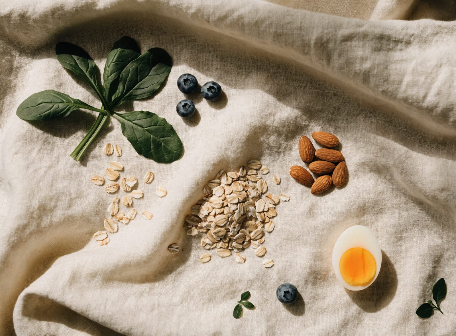 Spinach, blueberries, oats, almonds, and a soft-boiled egg arranged on cream linen